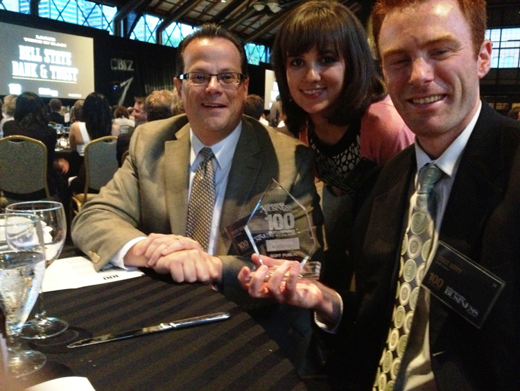 Three people smiling and holding an award at a conference