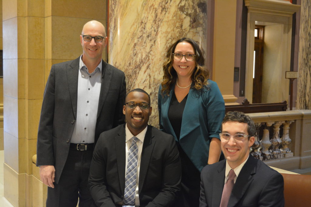 Four people smiling at the camera in front of a large marble pillar