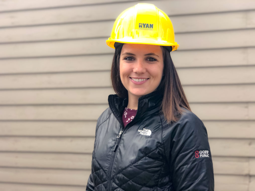 Close-up of a woman with short, brown hair smiling and wearing a construction hat