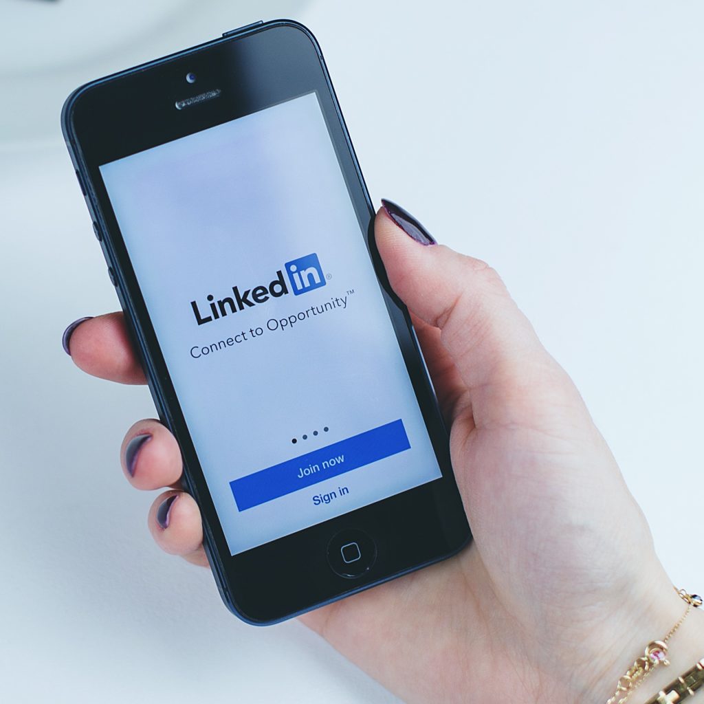 Hand holding a phone with the phone display showing the LinkedIn logo