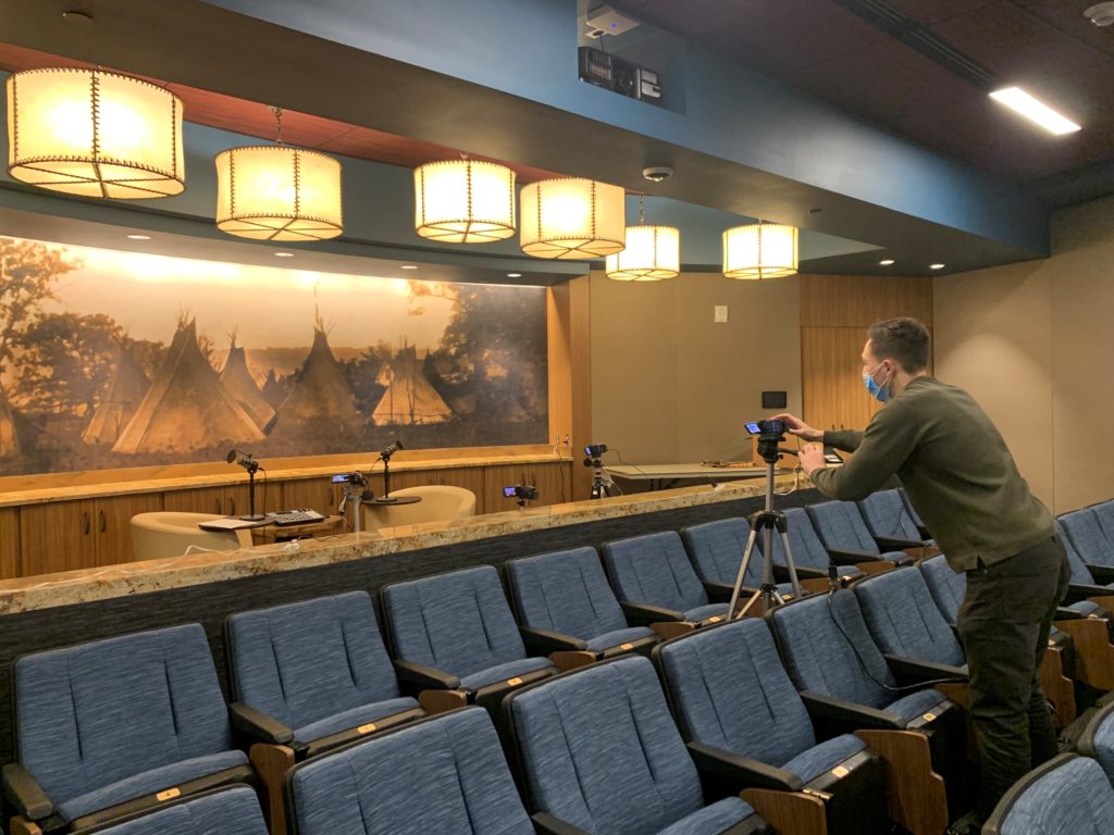 Small auditorium with chairs and a man operating a camera on a stand