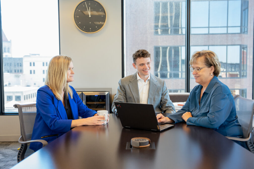 Three white professionals talk at a conference room table