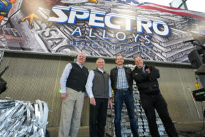 Four white men stand in front of a mural that says Spectro. 
