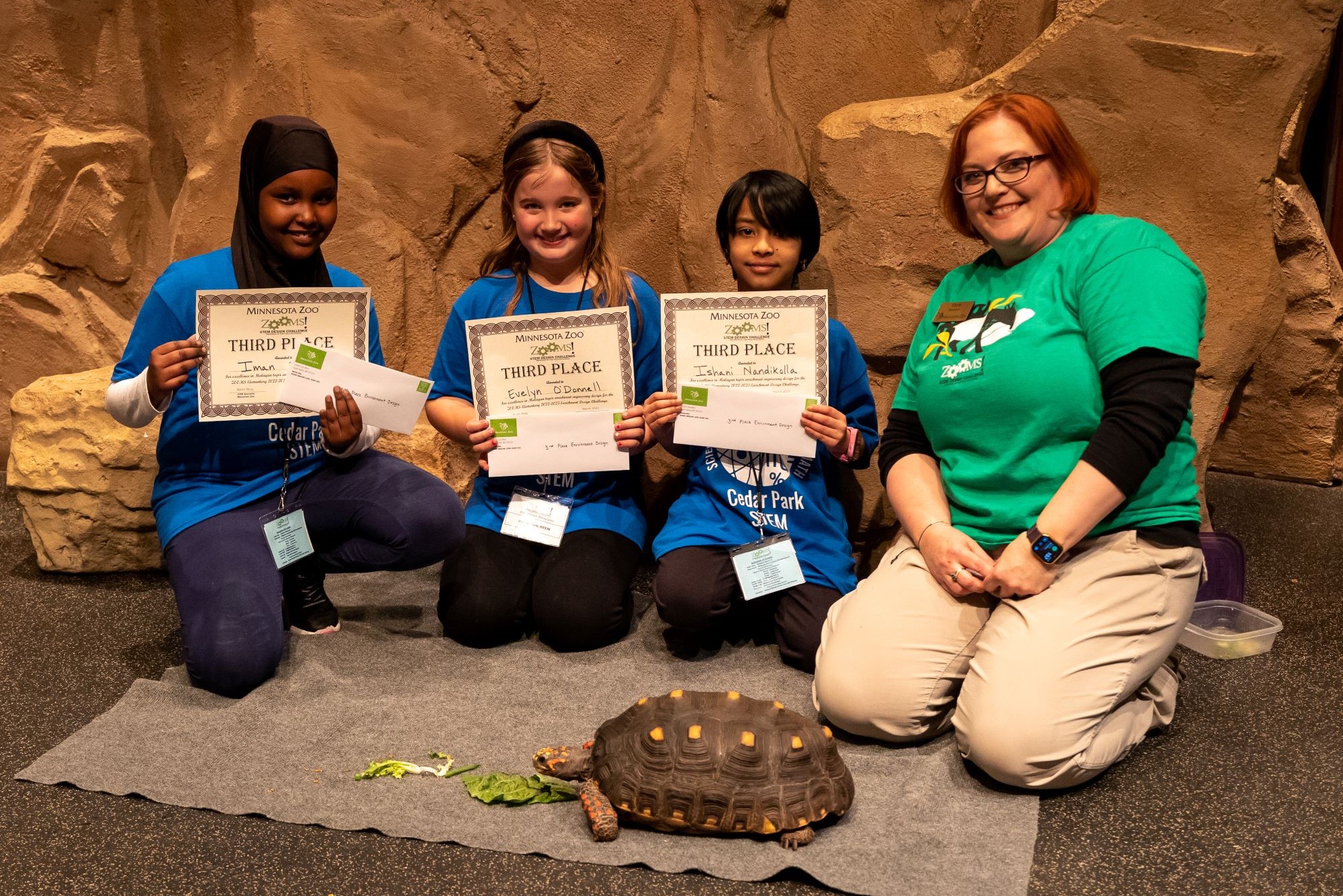 Three students and an adult showing off certificates in front a turtle.