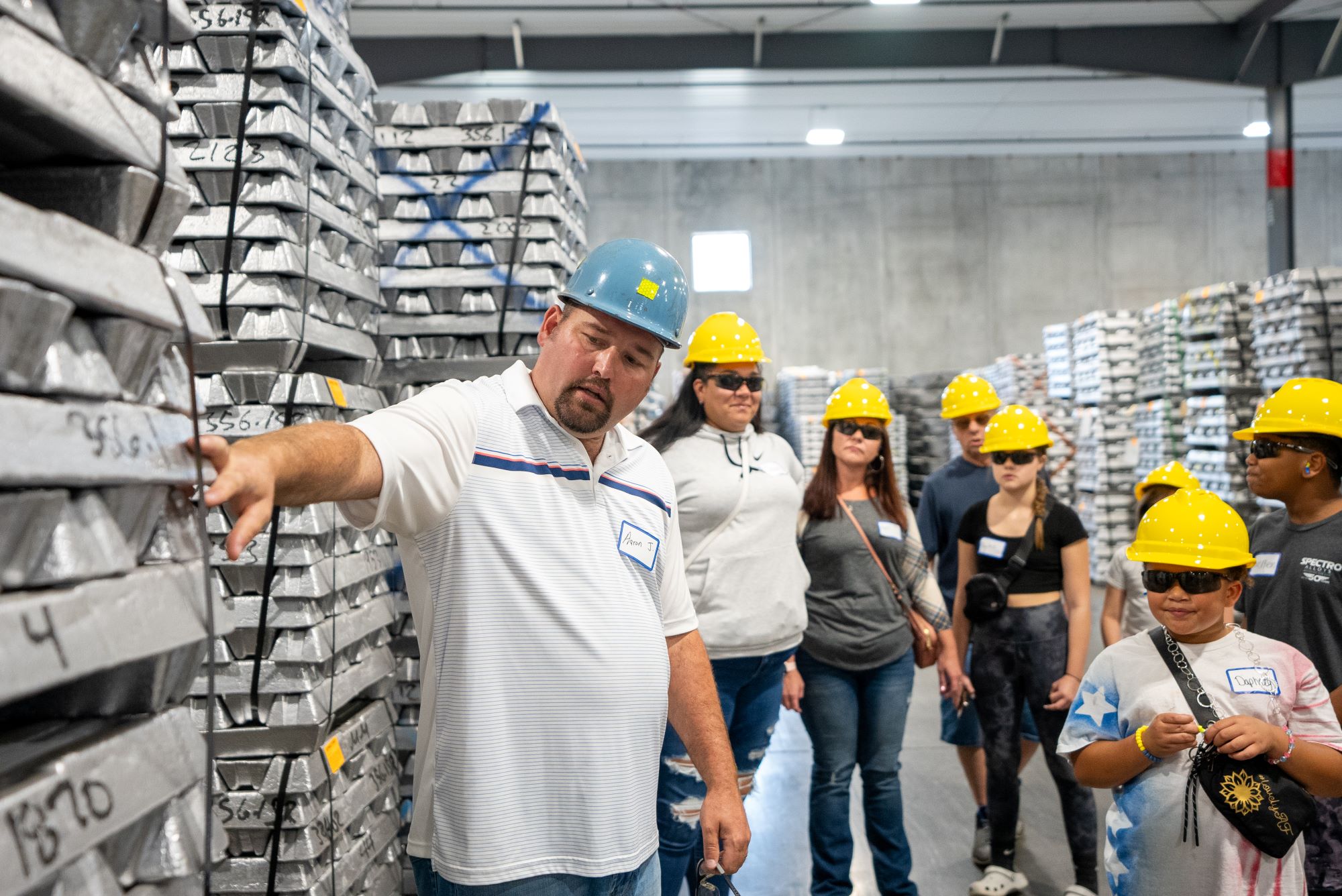 A man in a hardhat shows metal ingots to a group of people.