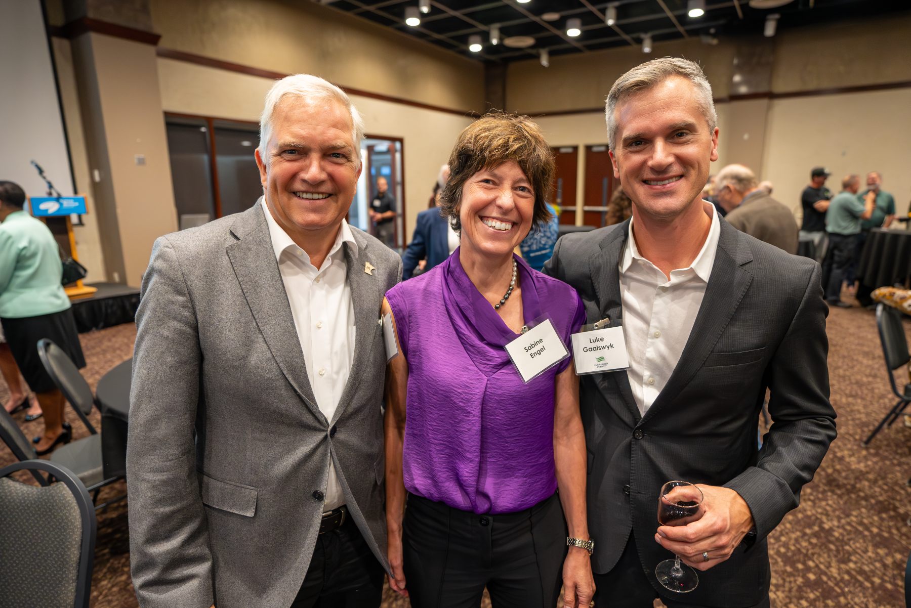 Three professionals in business clothes pose for a photo at an event.