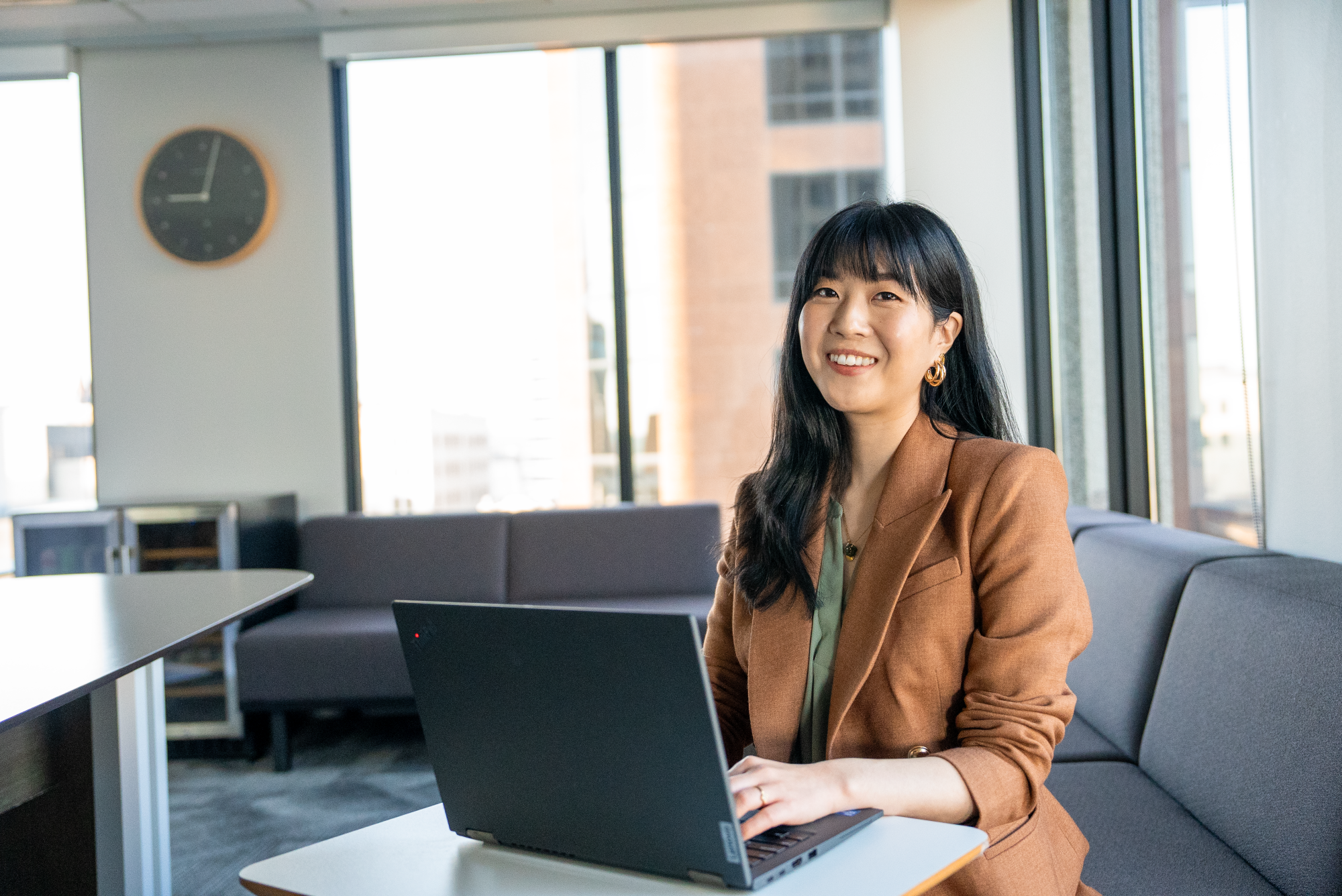 An Asian woman in a brown business coat sitting in front of a laptop.