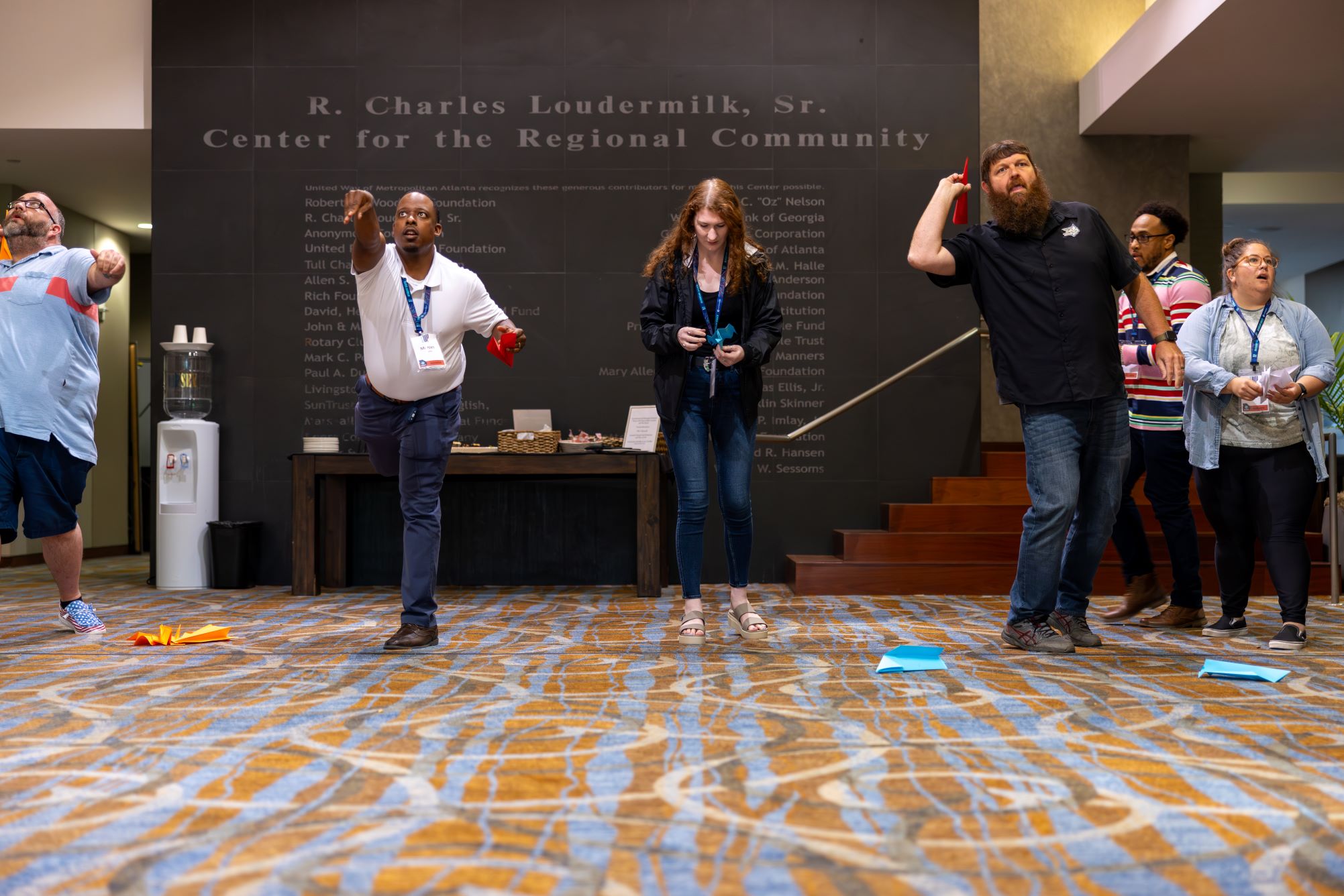 A group of people throwing paper airplanes in a lobby setting.