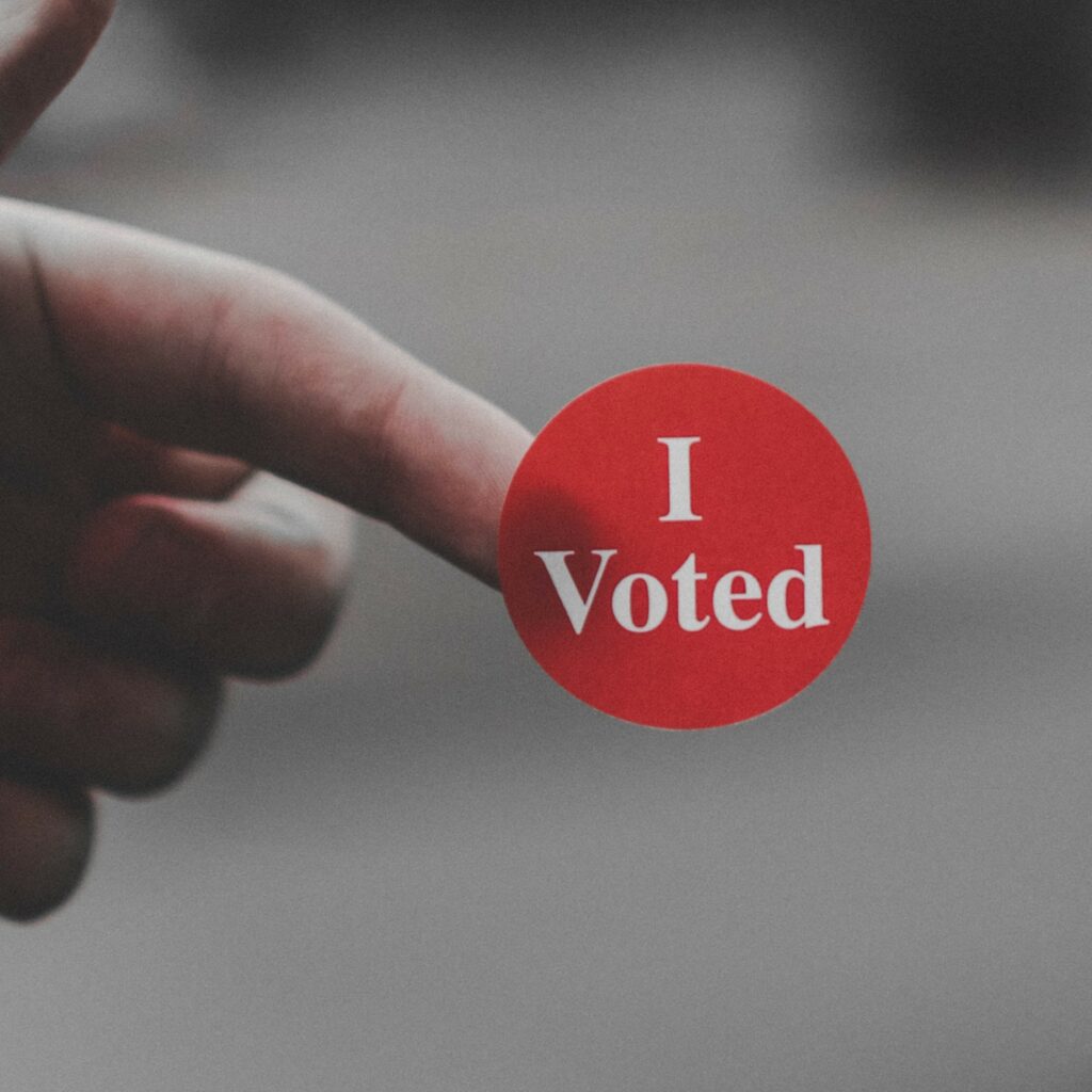 A finger holding a red "I voted" sticker