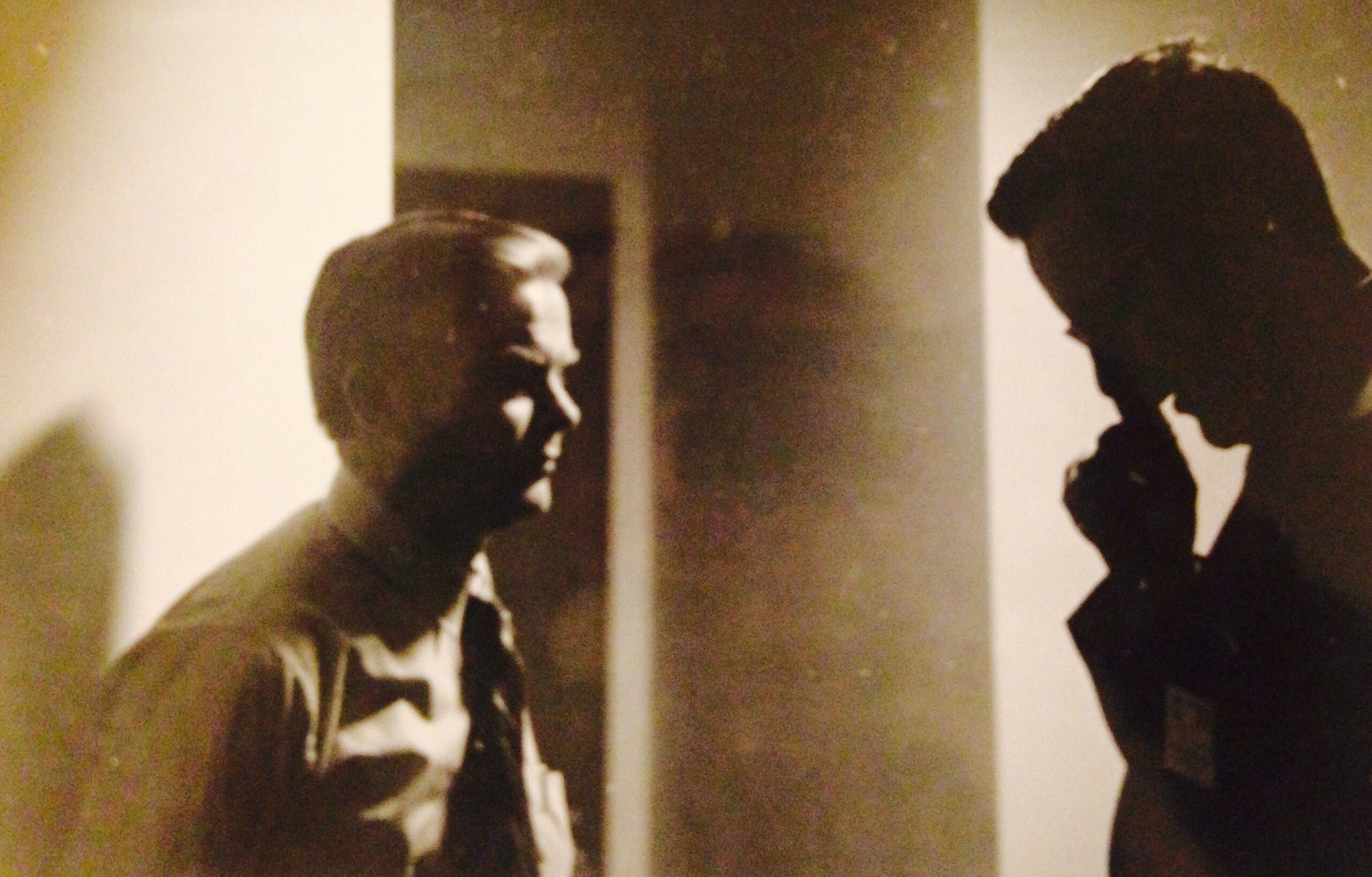 An old sepia image of men talking with each other in front of a doorway.