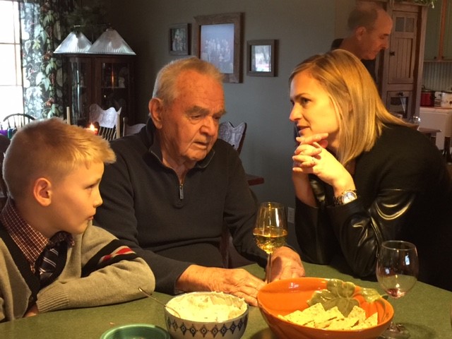 An old white man is engaged in conversation with a young blonde boy and a blonde woman.