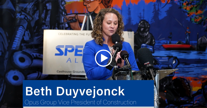 A woman in a blue suit speaks into a microphone at a podium