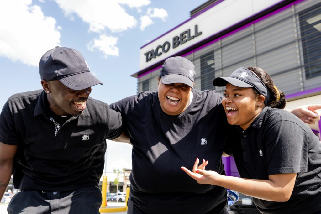 Three Taco Bell employees laugh outside Taco Bell Defy.