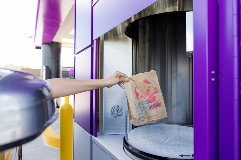 A hand puts a Taco Bell bag of food into a cylinder for delivery.
