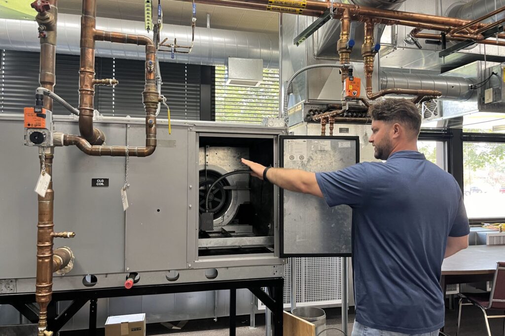 A man in a blue shirt points out parts on an air ventilation system