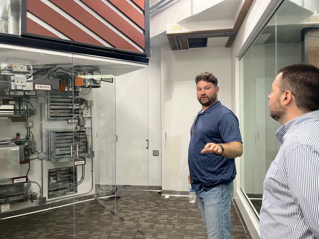 A man in a blue shirt shows air ventilation systems to another man in a white button down shirt