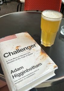 The book "Challenger" by Adam Higginbotham sits on a table next to a pint glass of beer