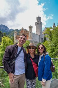 A young man, older woman and young woman pose in front of a castle in Europe