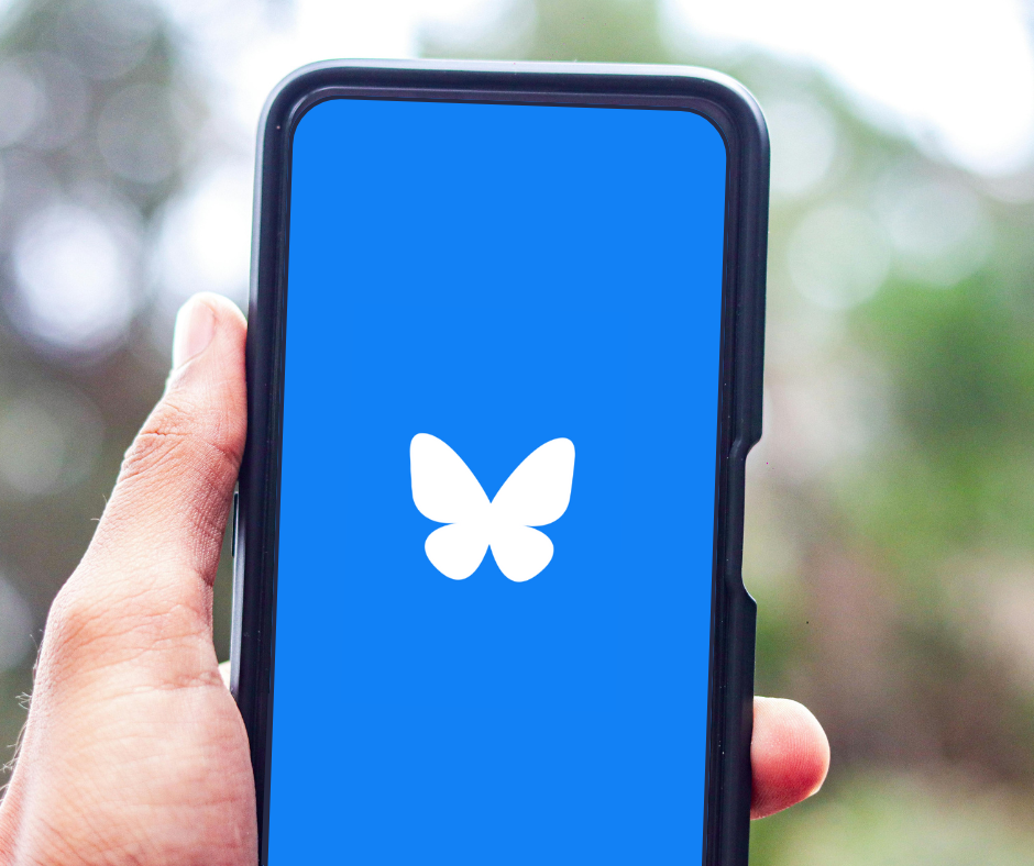 A hand holds a smartphone with the Bluesky login on the screen