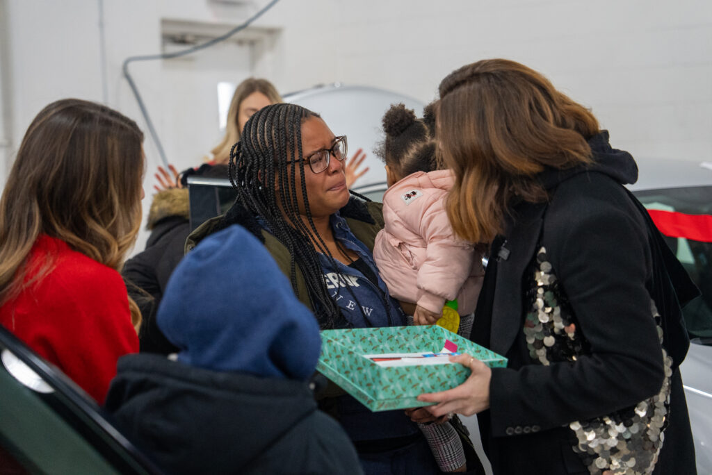 A mom holding a toddler accepts a present from a woman