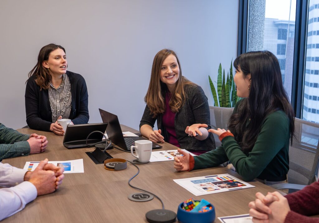 Three women talk animatedly in a conference room