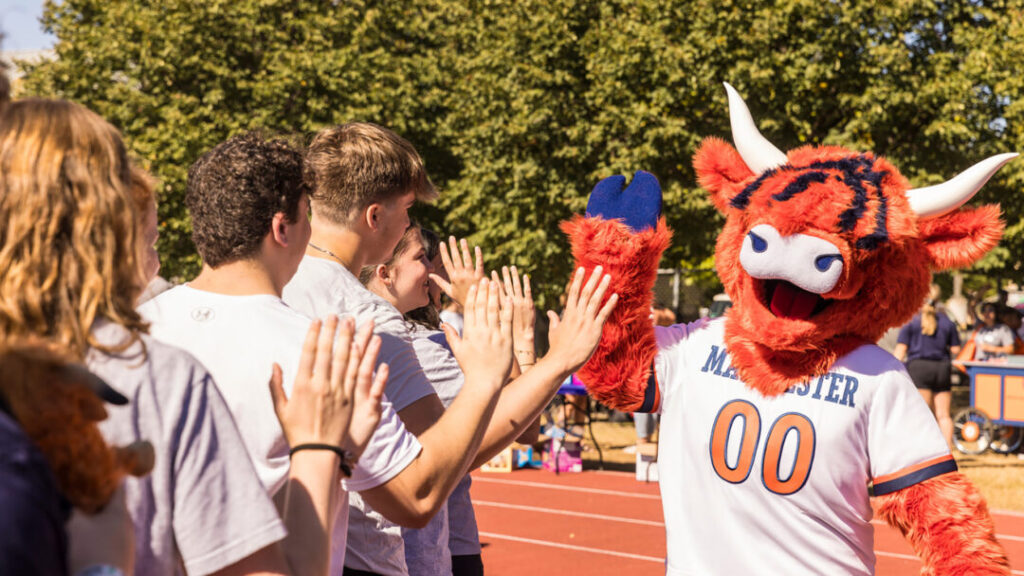 Macalester students high fiving a highland cow mascot