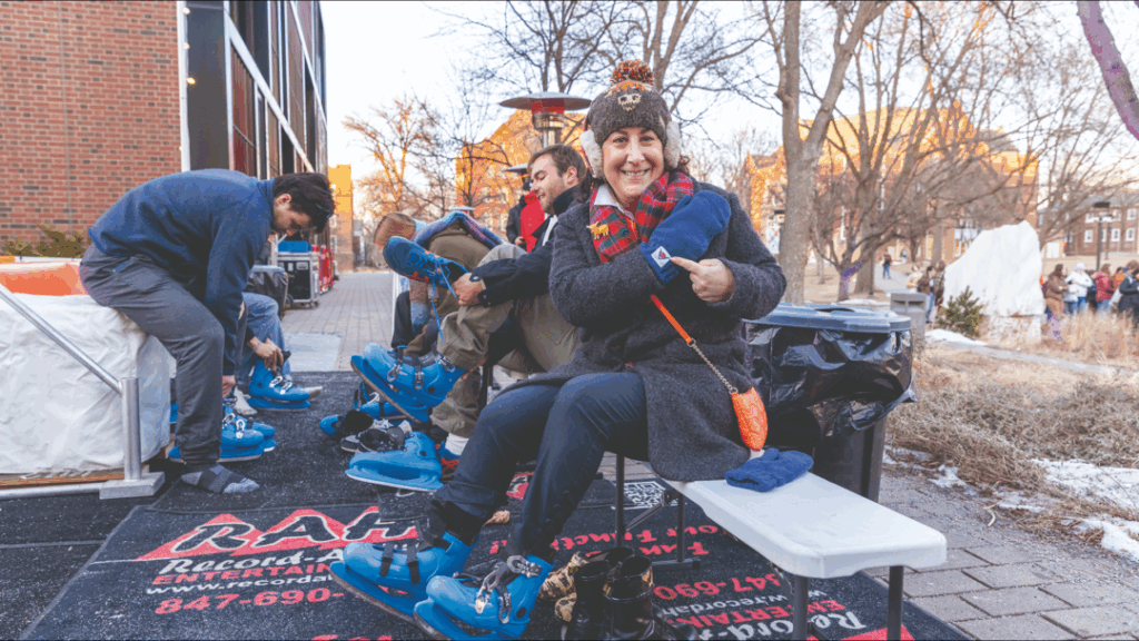 A Macalester alumni points to the college logo on her mitten while tying ice skates