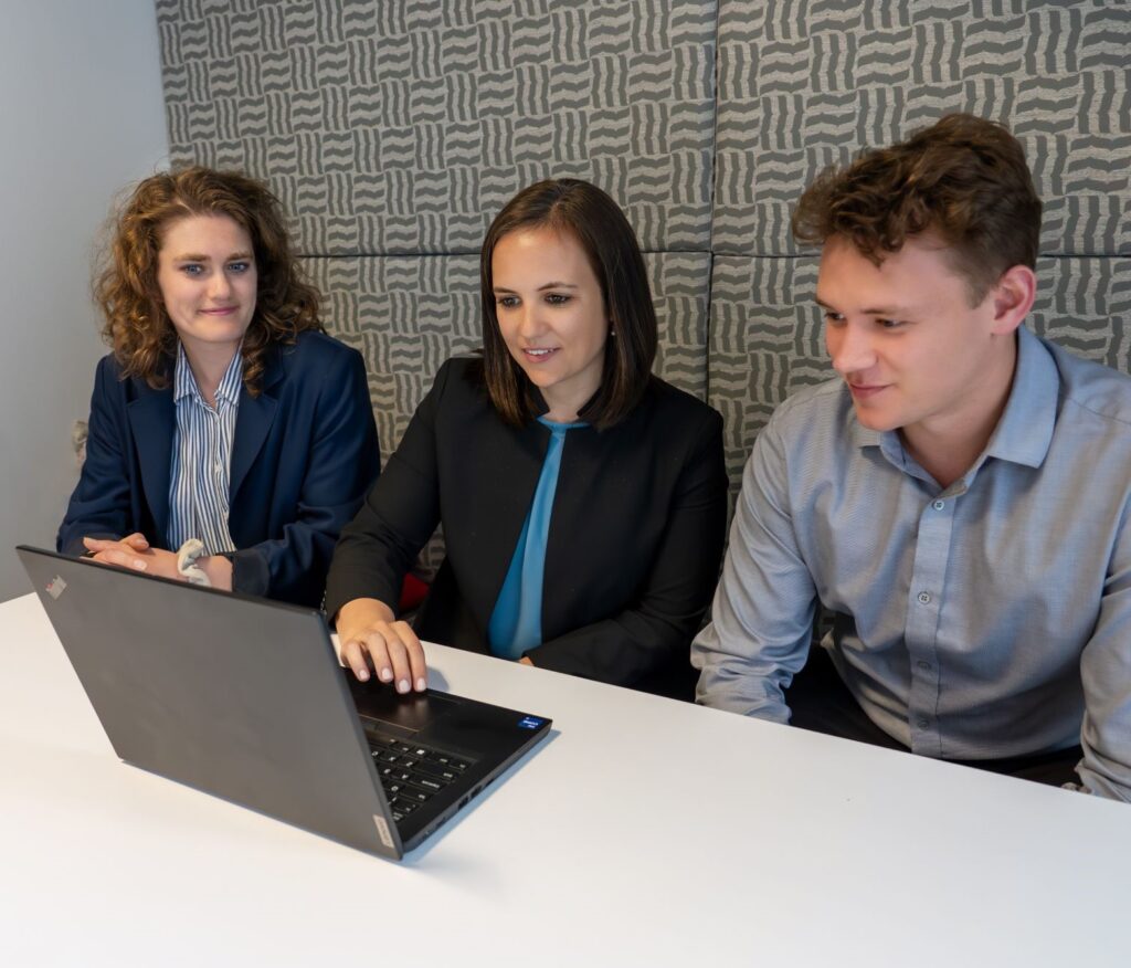 Three employees sit and talk in front of a computer in an office