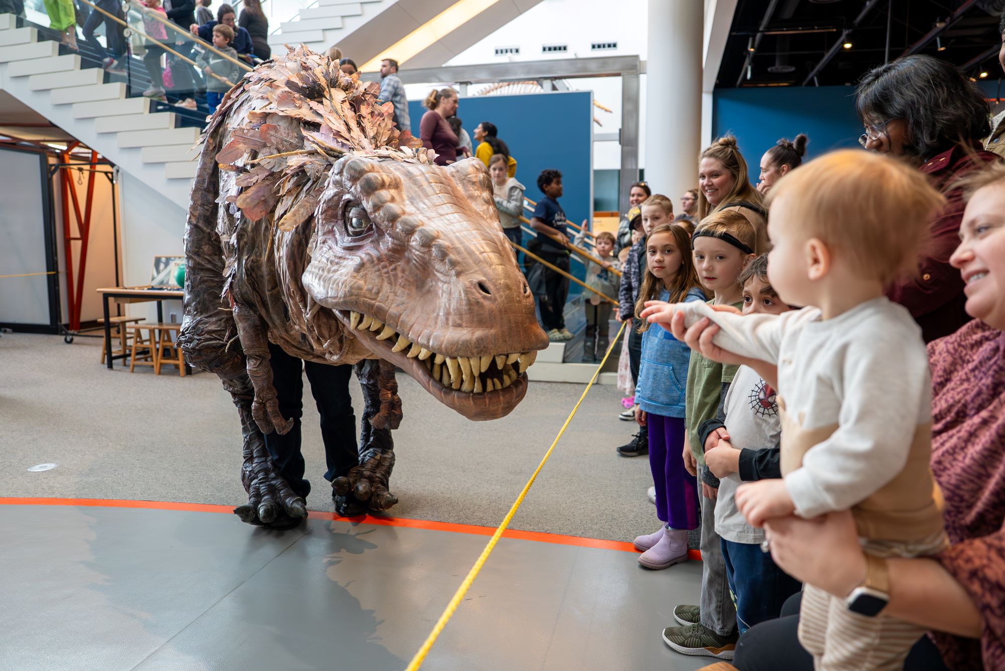 An animatronic T-rex entertains a crowd of children and parents