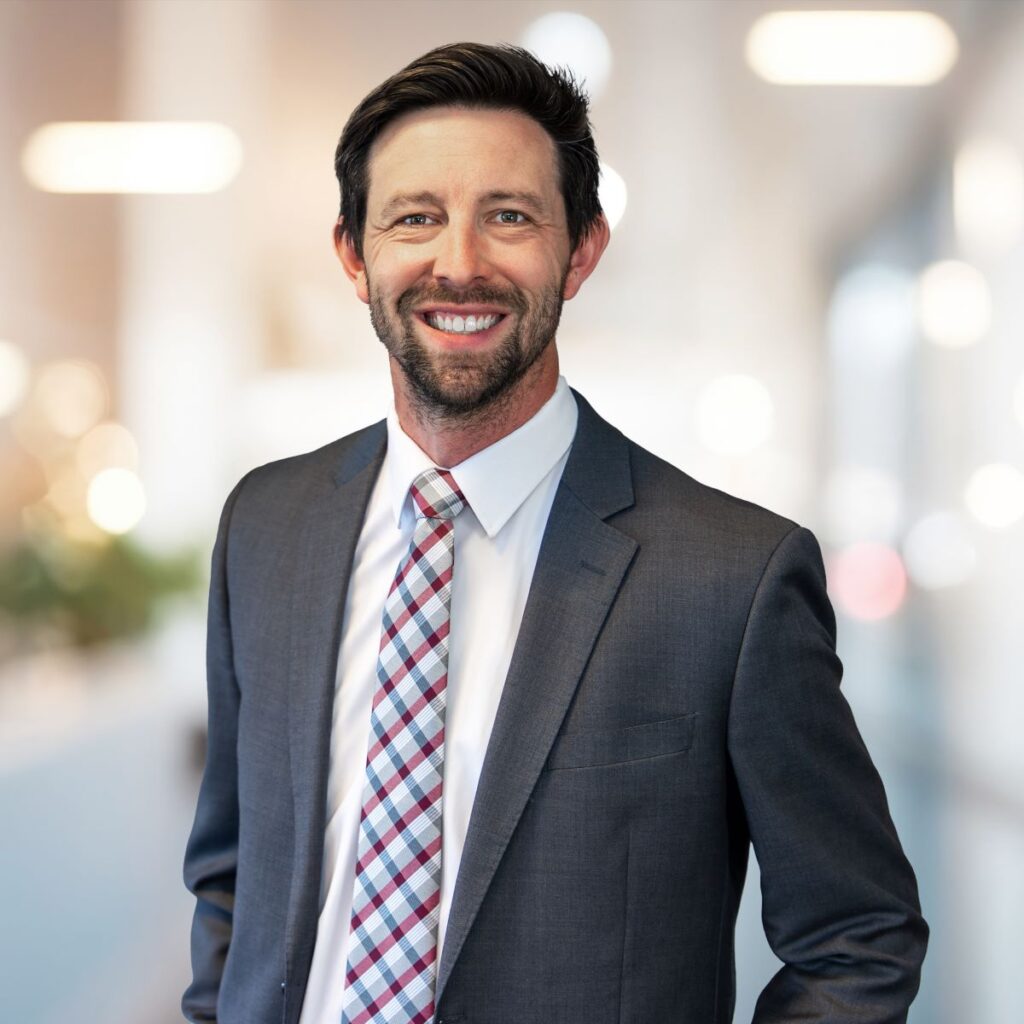 A man, Jake Ricker, in a suit poses for a headshot.